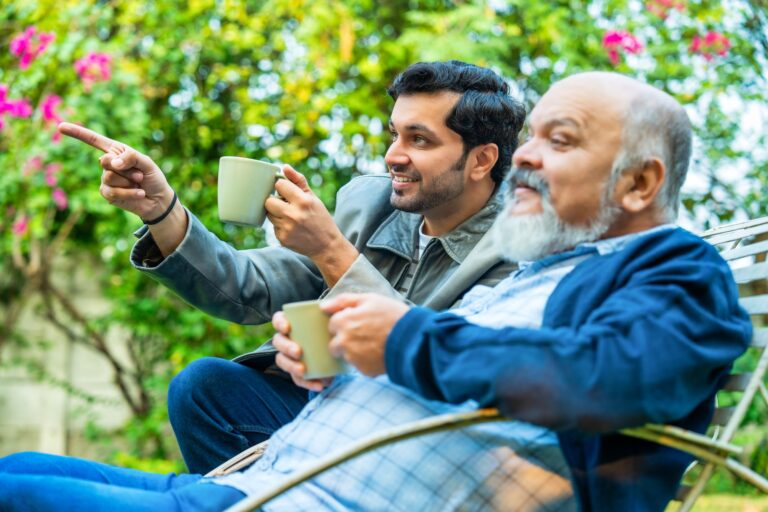 Closeup of an elderly father and young adult son relaxing together in a home garden, smiling warmly